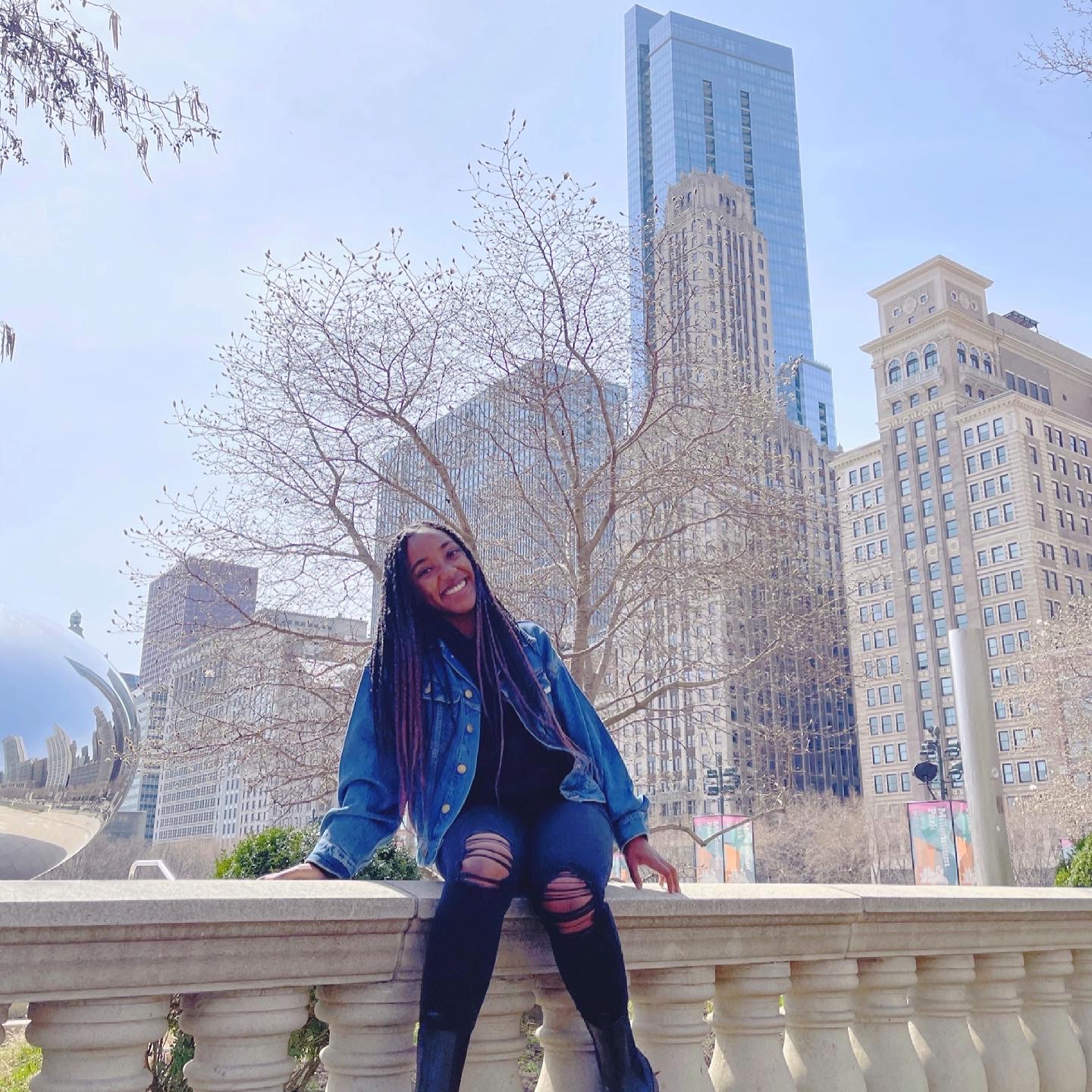 Kayla Landers sitting on a stone-column railing with a city skyline in the background