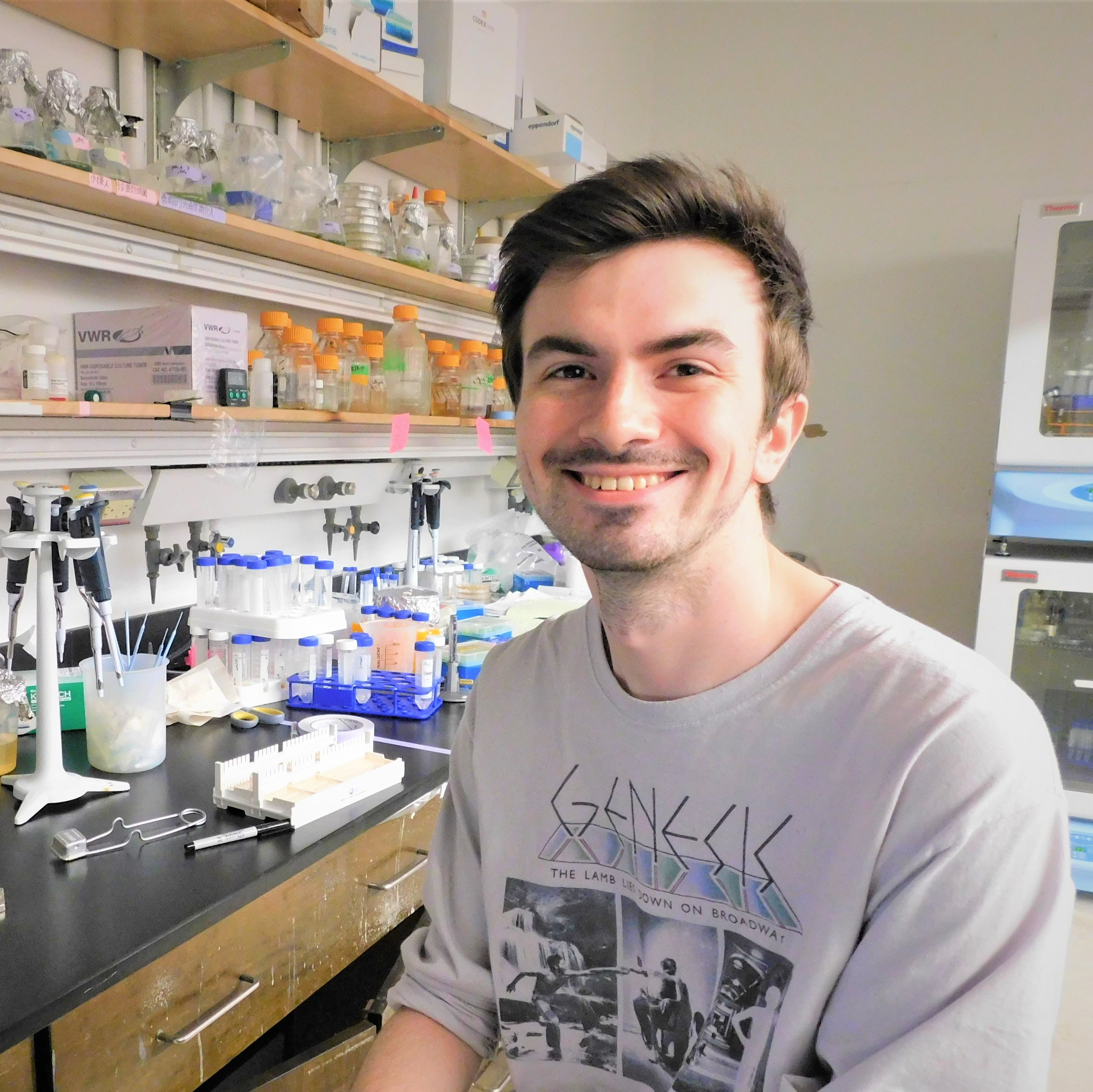 Photo of Jason sitting on a stool at a bench in a chemistry lab on campus.