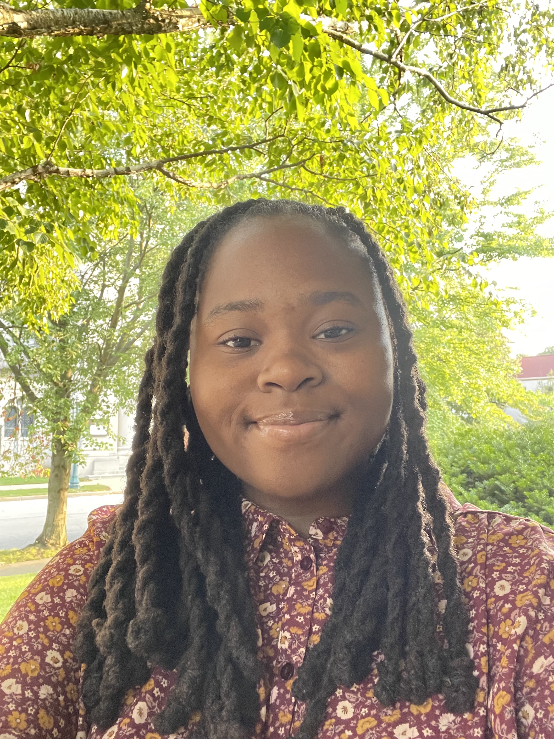 Head shot of Sophia Marcellus in an outdoor setting with green leaves of trees in background