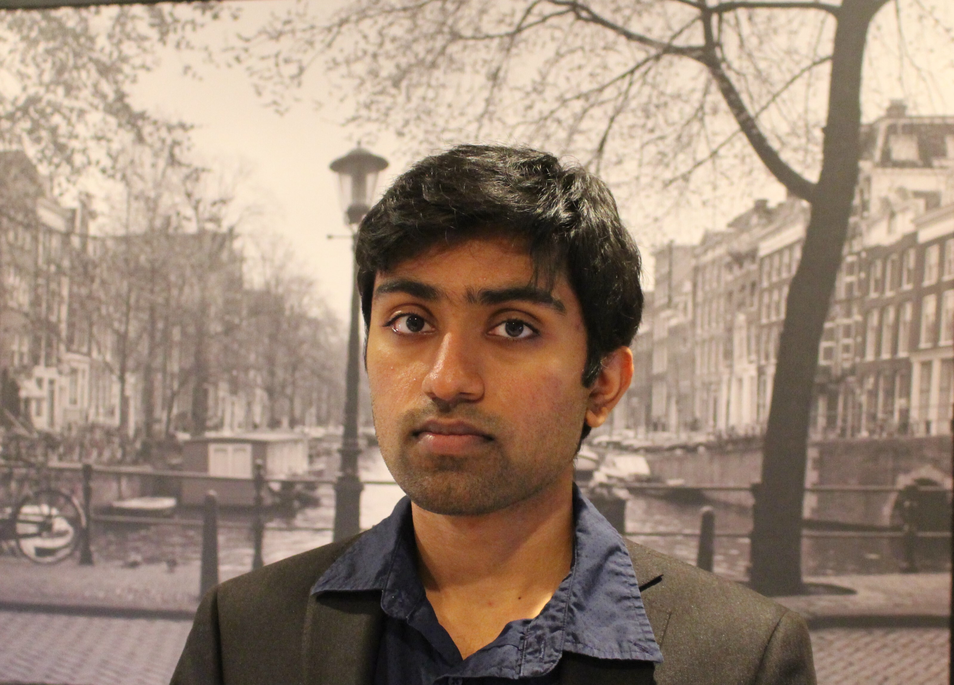 Head shot of Swaroop Thammineni standing in front of a large black and white photographic mural of a downtown scene. 