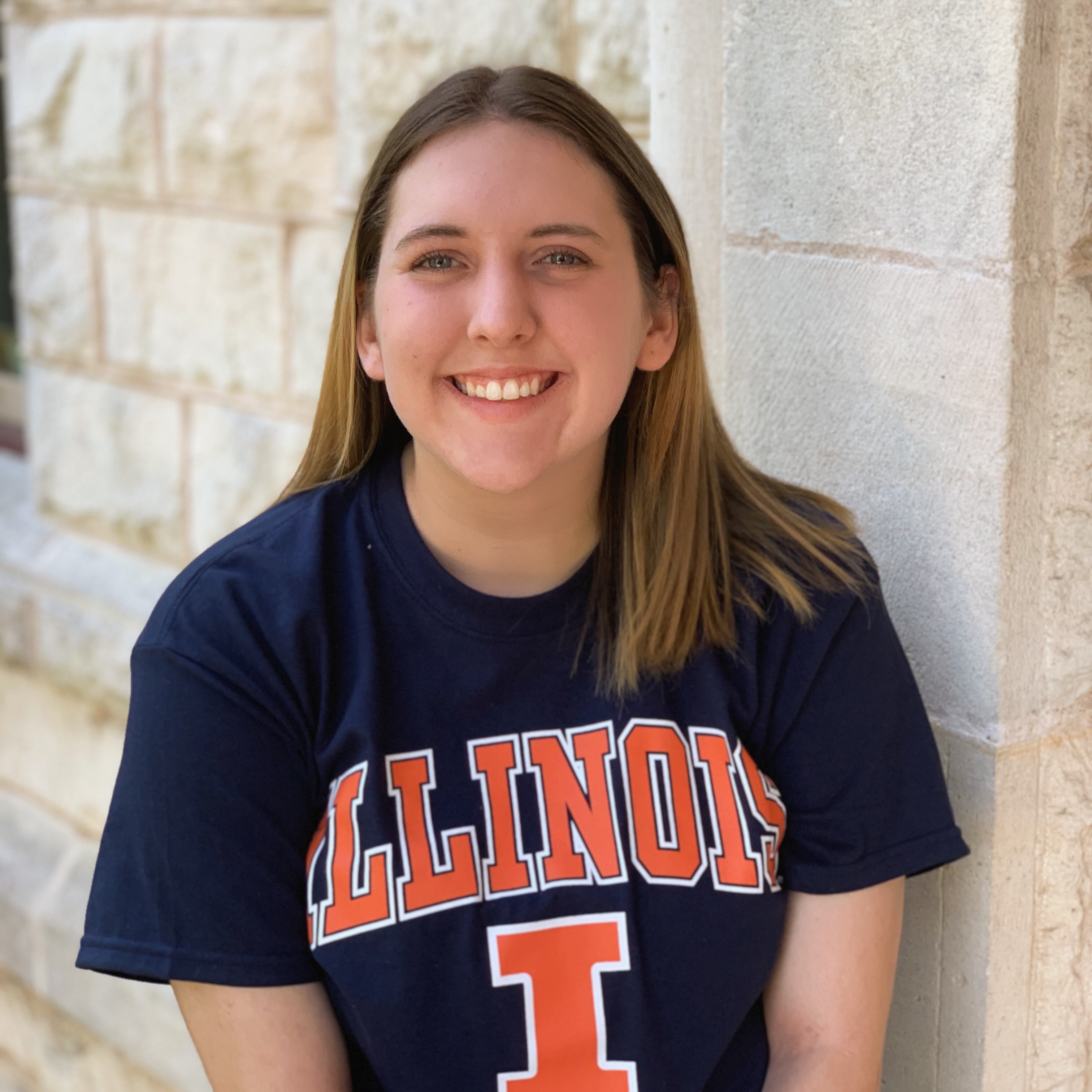 Portrait of Glenn Blade wearing a blue and orange Illinois t-shirt standing in front of a brick wall.