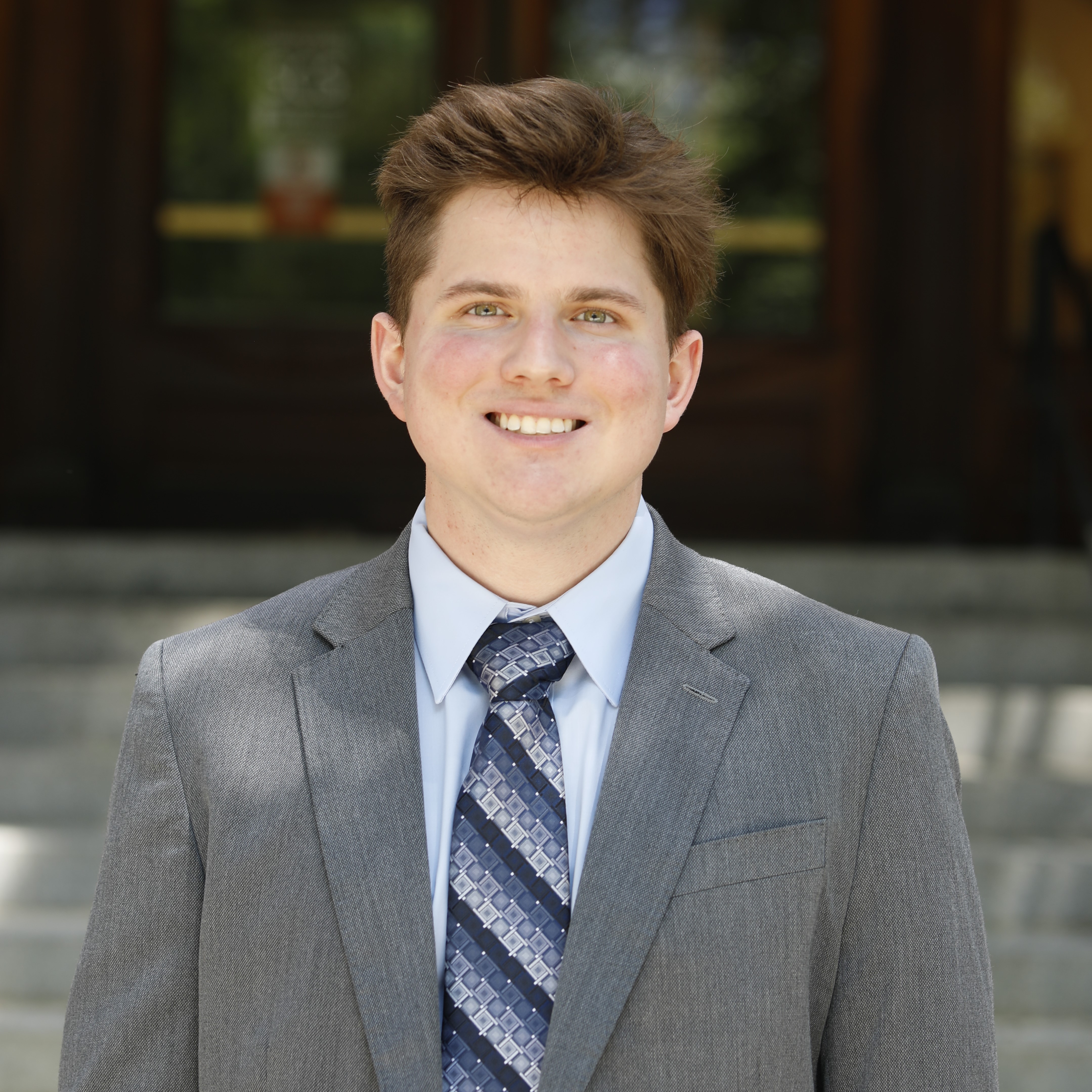 Portrait of Seth Klaine in a suit jacket and tie standing in front of Noyes Laboratory's main entrance.