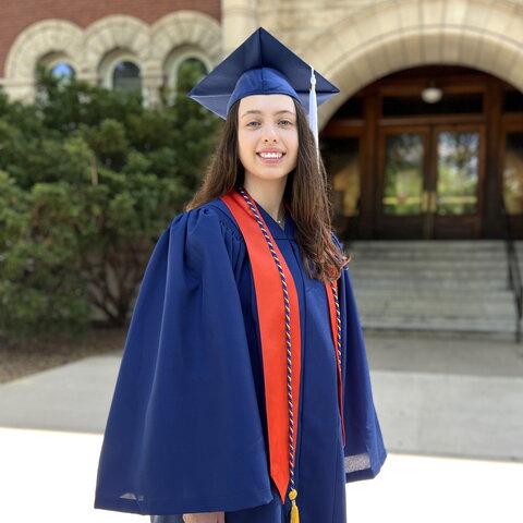 Portrait of Morgan Kennebeck in graduation regalia standing in entrance to Noyes.