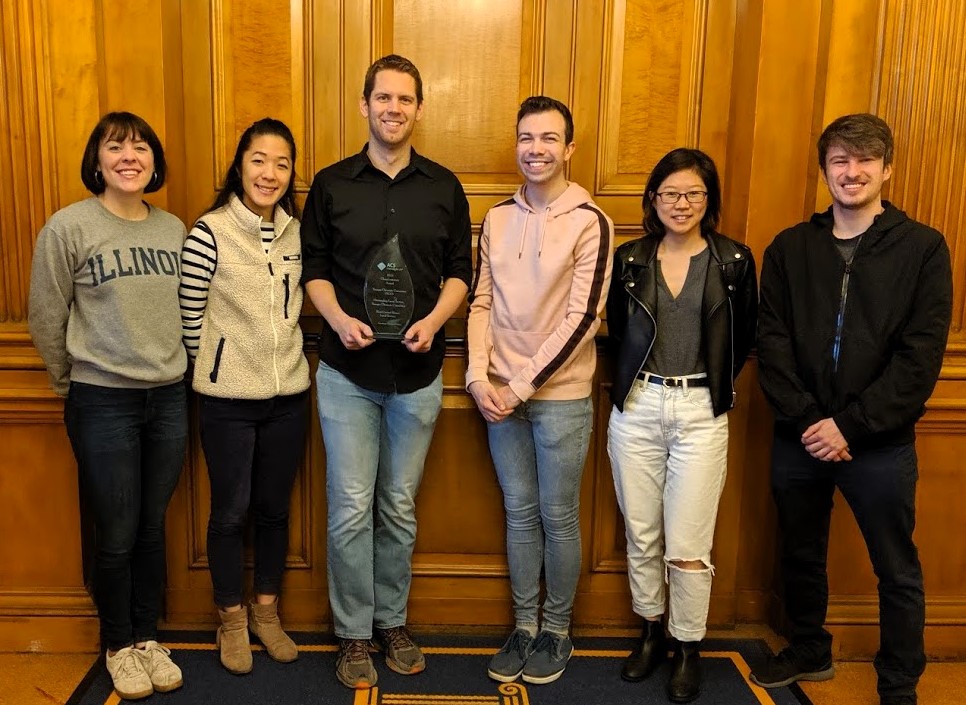 Six members of YCC stand side by side in front of a brown wall with one student holding the ChemLuminary award.