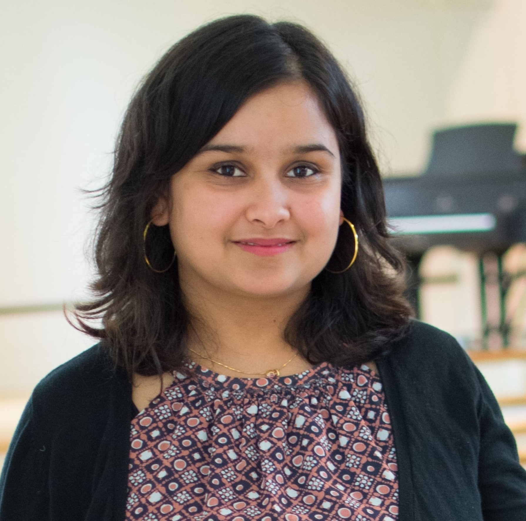 Head shot of Priti Kharel on a white background with a piano in the background