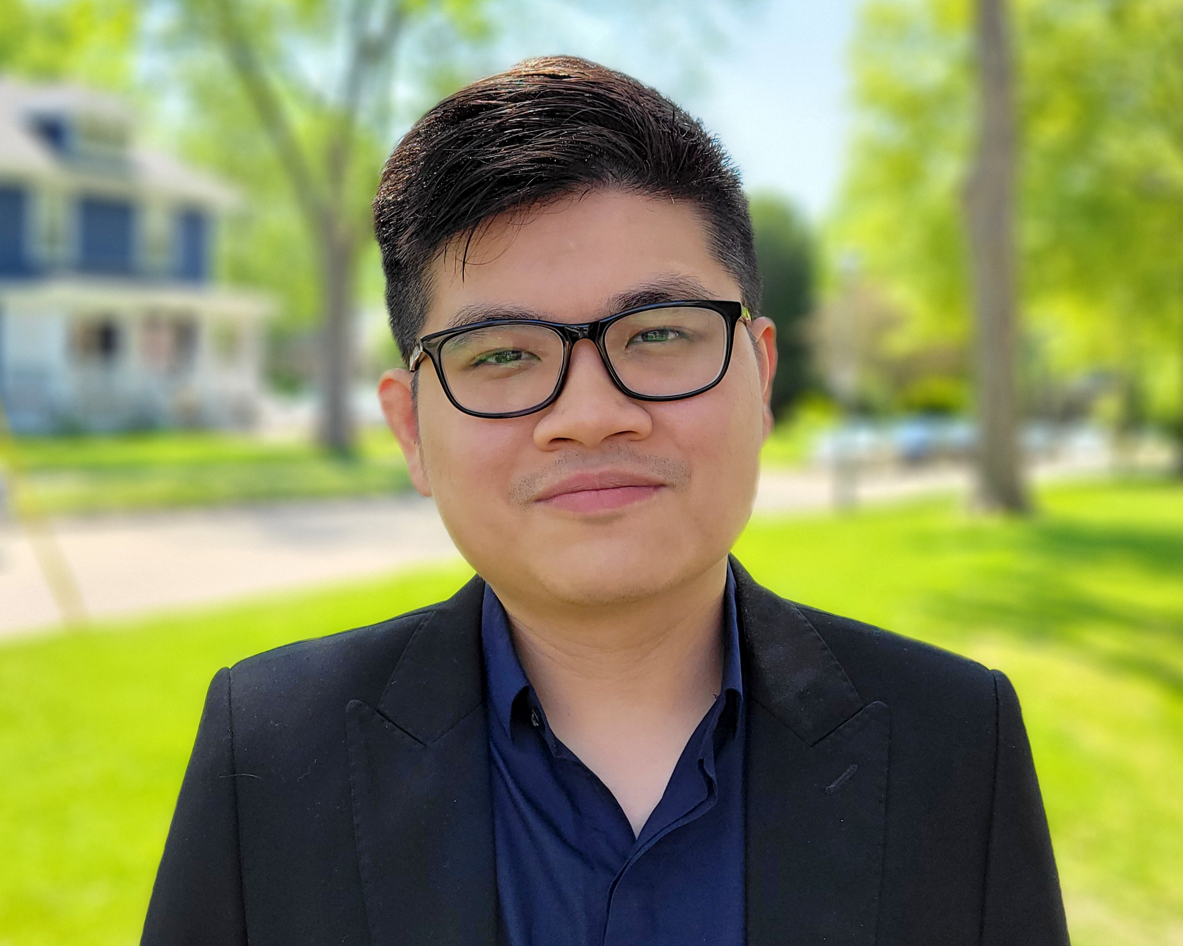 Head shot of Dinh Nguyen in an outdoor setting with a street, tree and house in the background