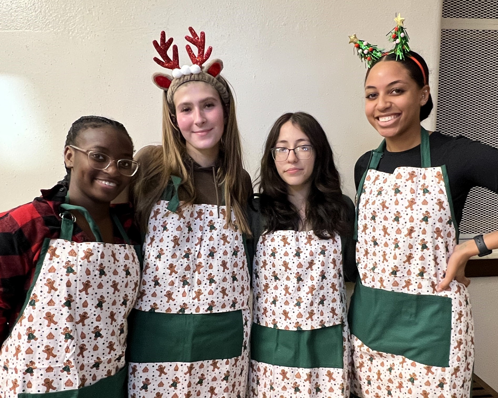 Four students in holiday aprons stand side by side in front of a white wall.