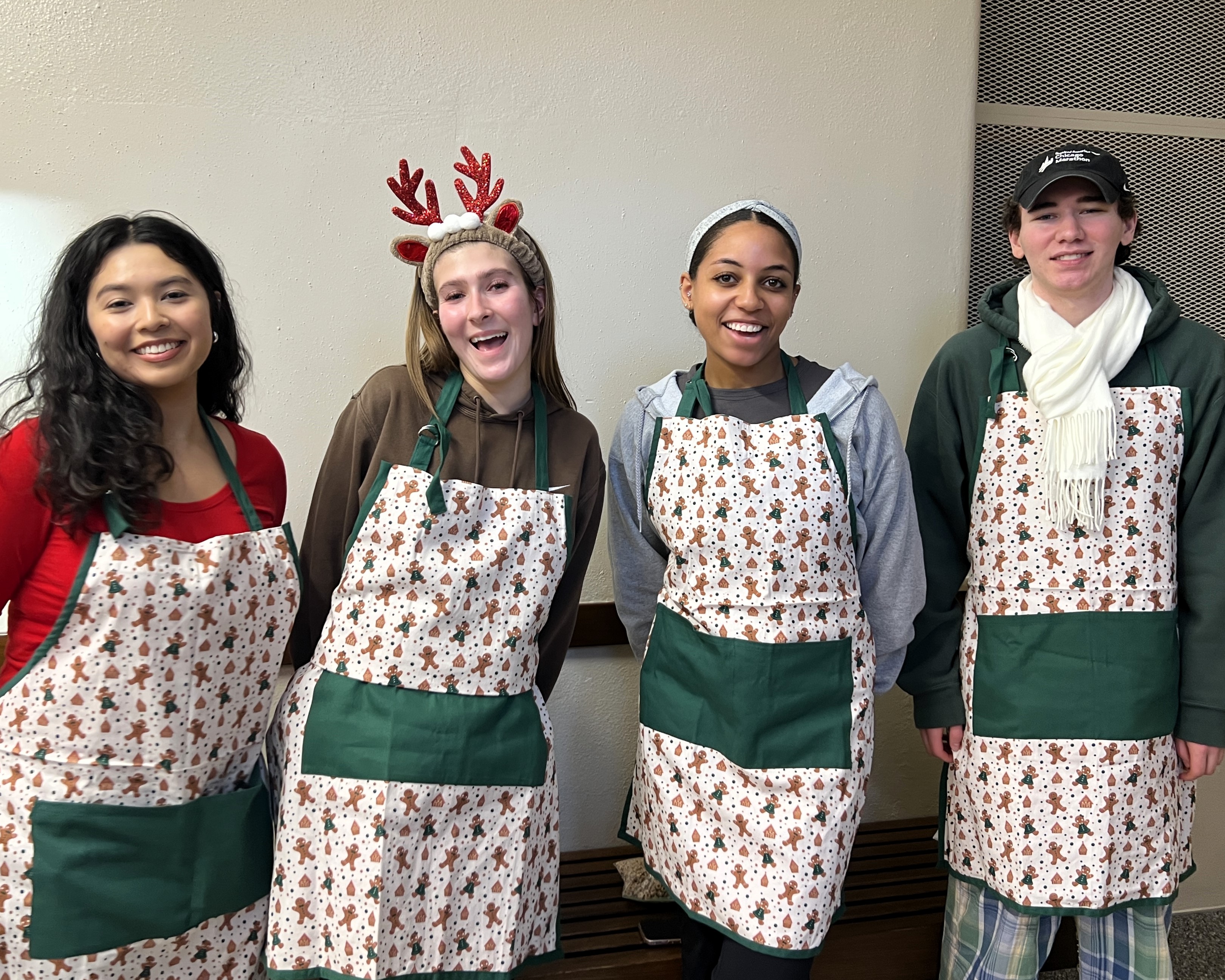 Four students with holiday aprons stand side by side in the hallway.