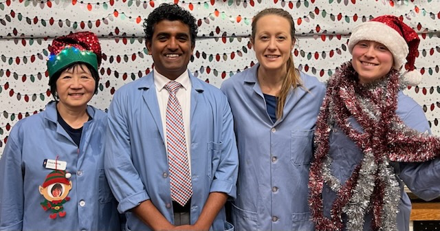 Four people in lab coats and holiday accessories stand side by side