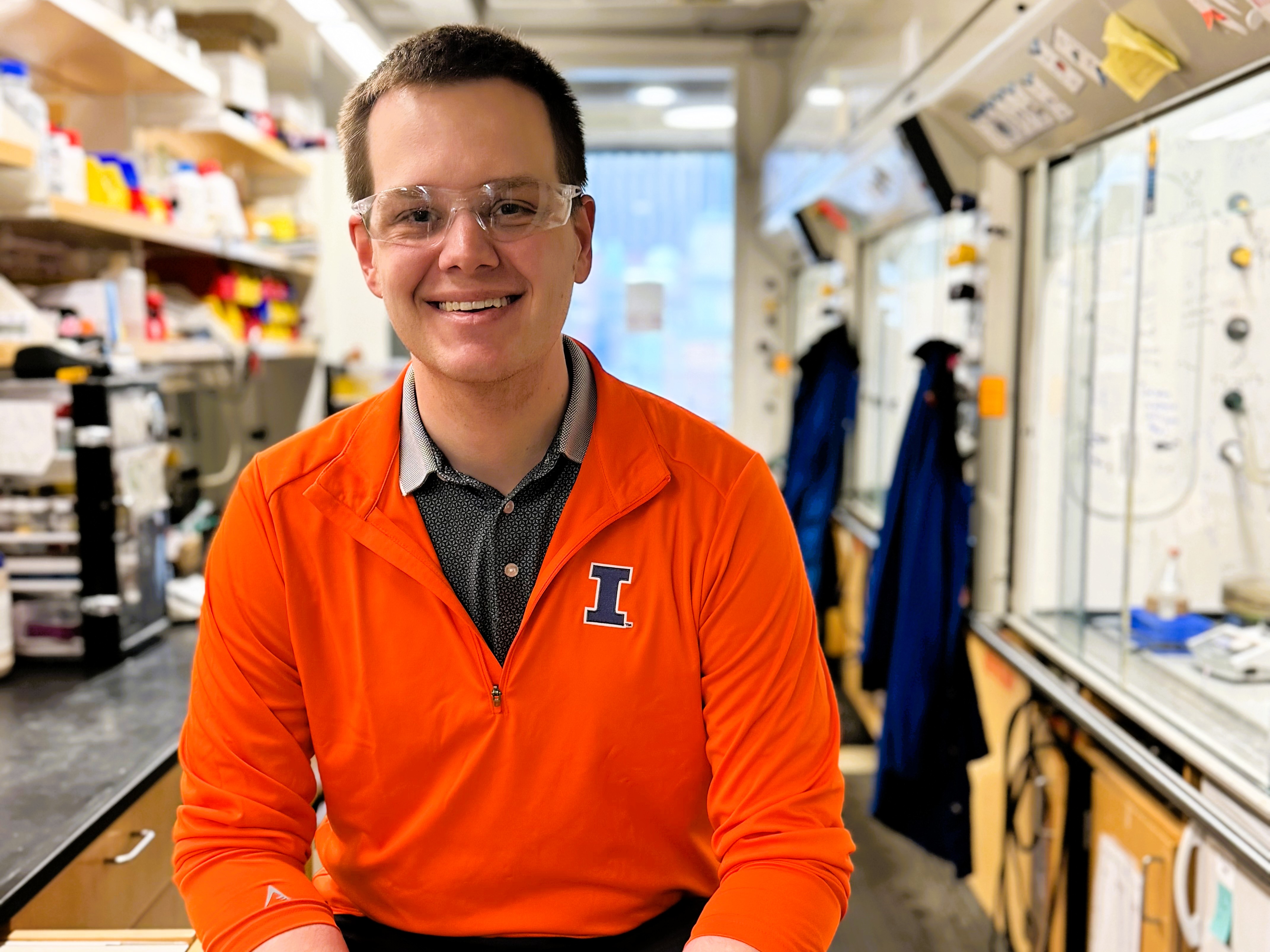 Mike Strauss sitting on a table in a lab on campus wearing an orange Illinois shirt.