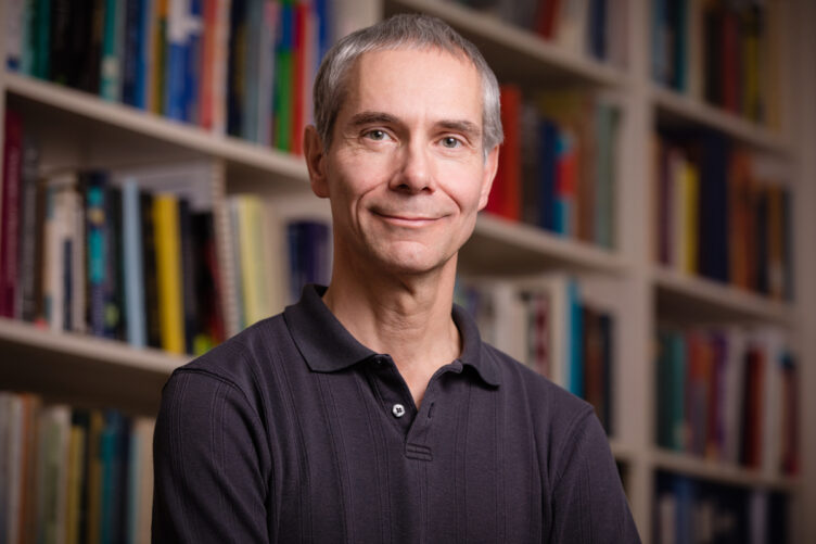 Martin Gruebele posed in front of a wall of shelves filled with books
