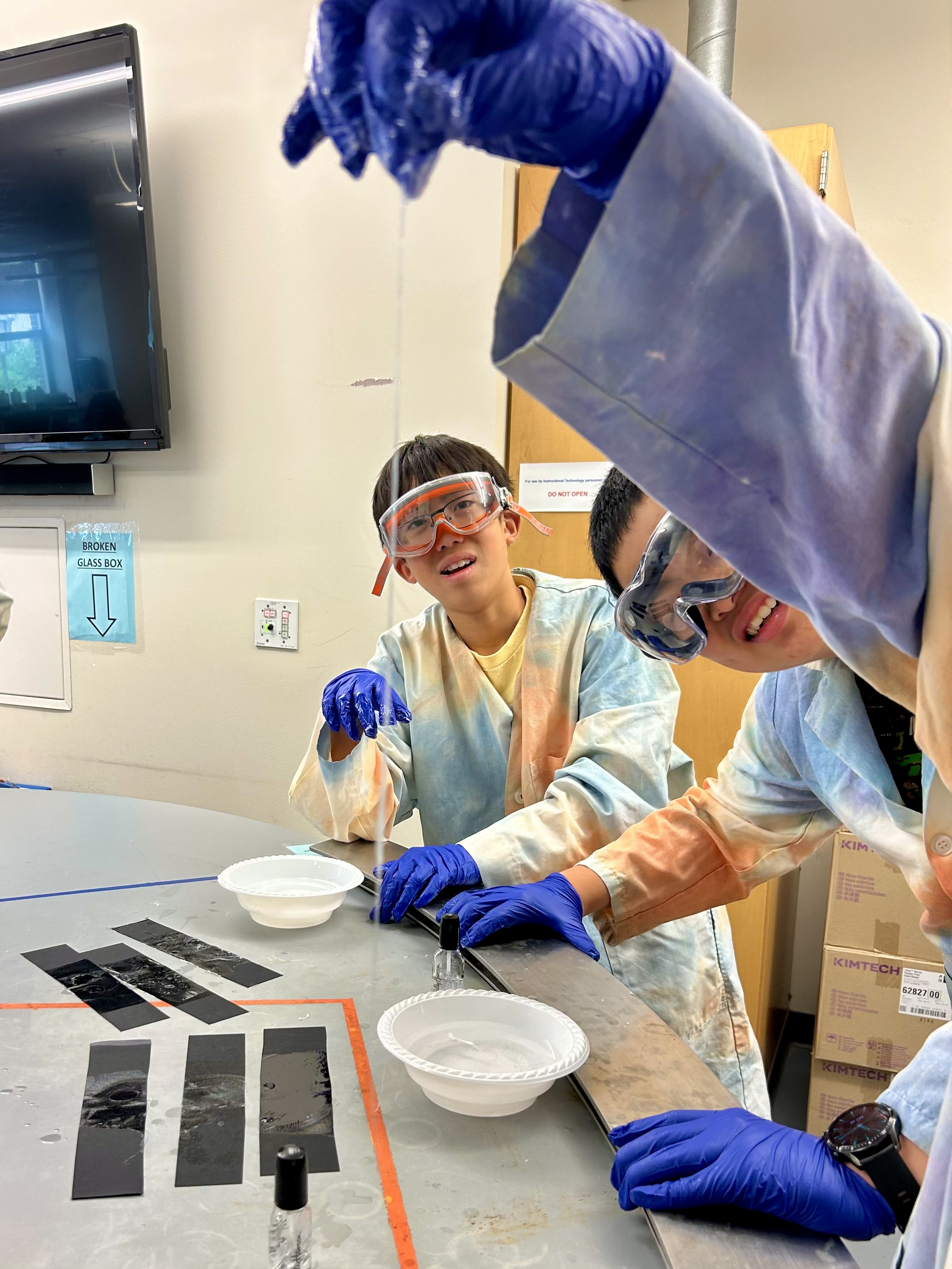 Two kids in lab coats and goggles looking at a stretched thin film