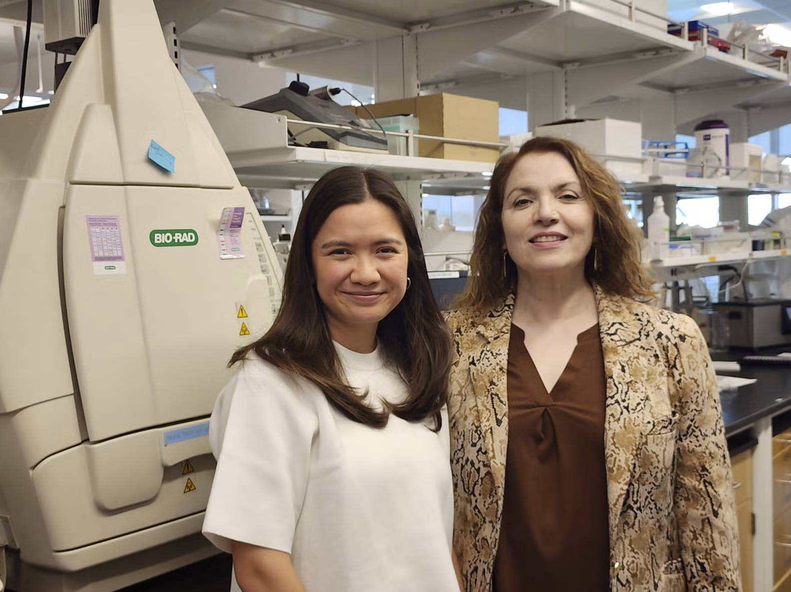 Photo of two women standing together in front of equipment in a lab