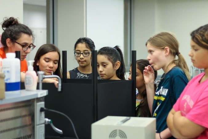 Six girls watch as a volunteer explains their next task.