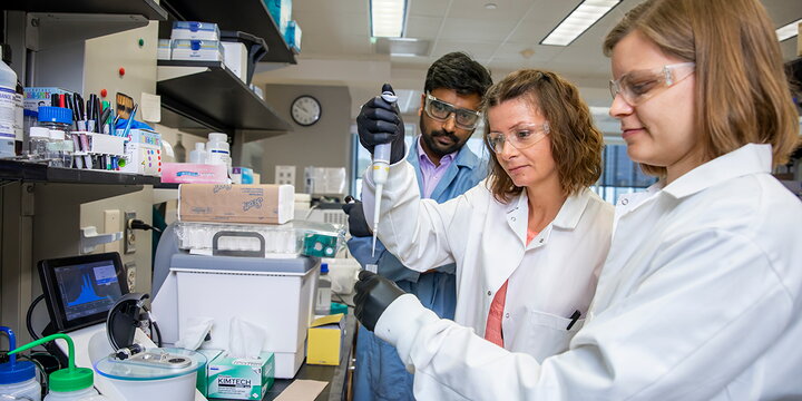 Three chemists in lab using dropper to fill vial