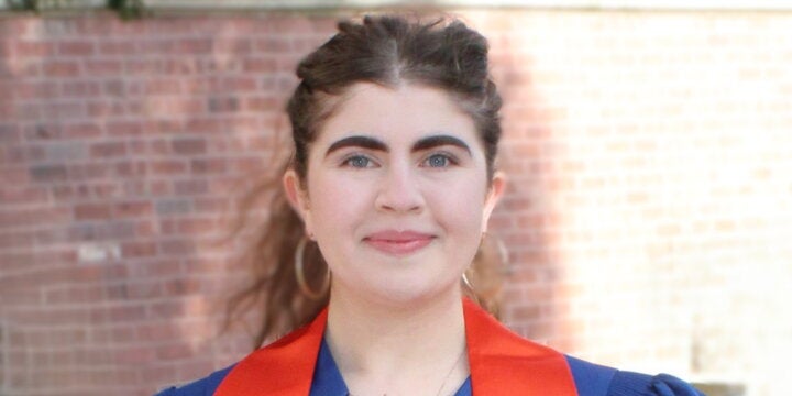 Michaela Klein in a graduation gown in front of a brick wall