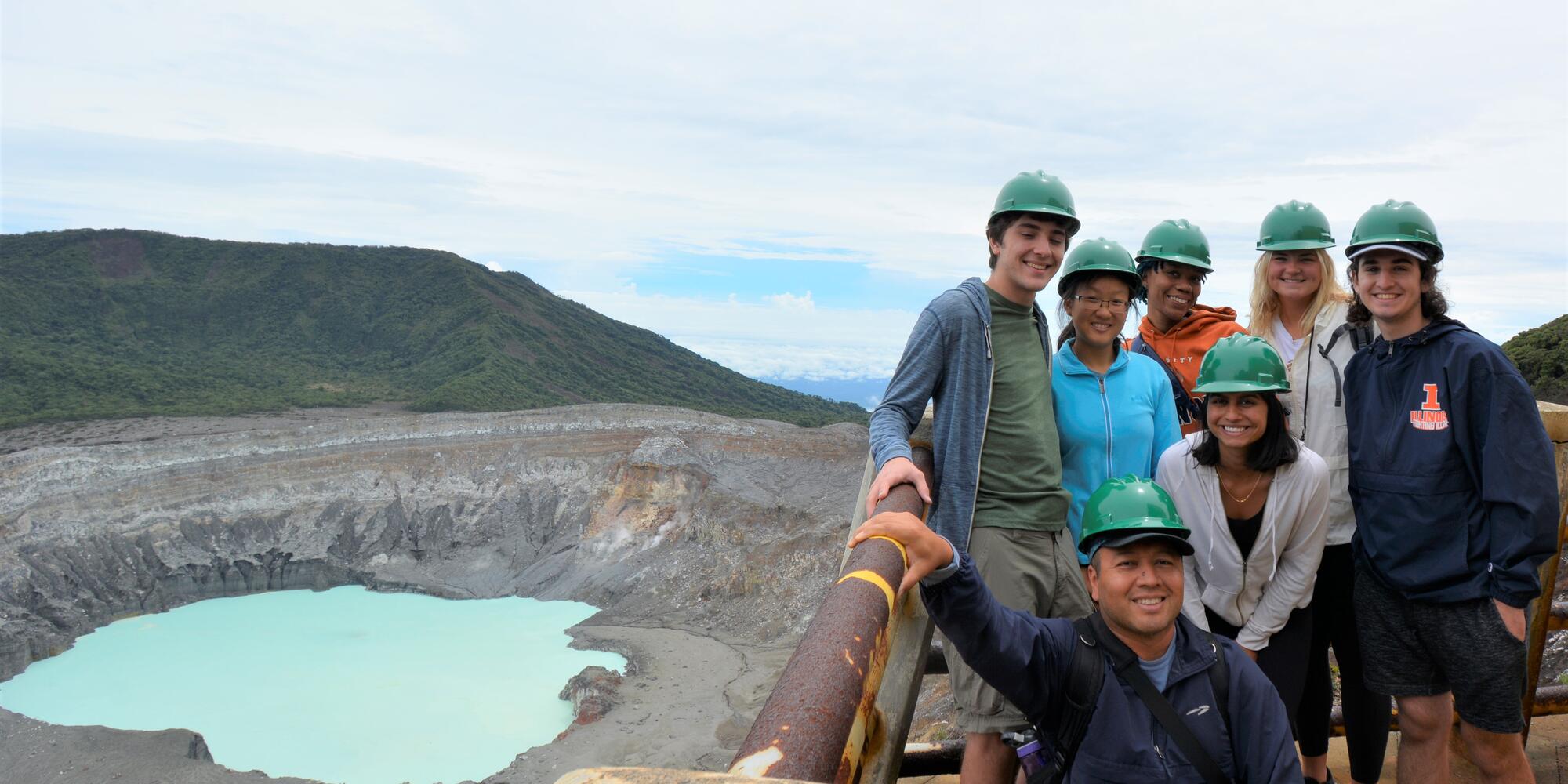 Group of students wearing hard hats stand on ledge overlooking a water body in Costa Rica with wear