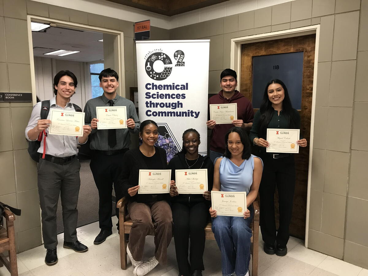 Seven students gathered around a vertical C2 banner holding certificates