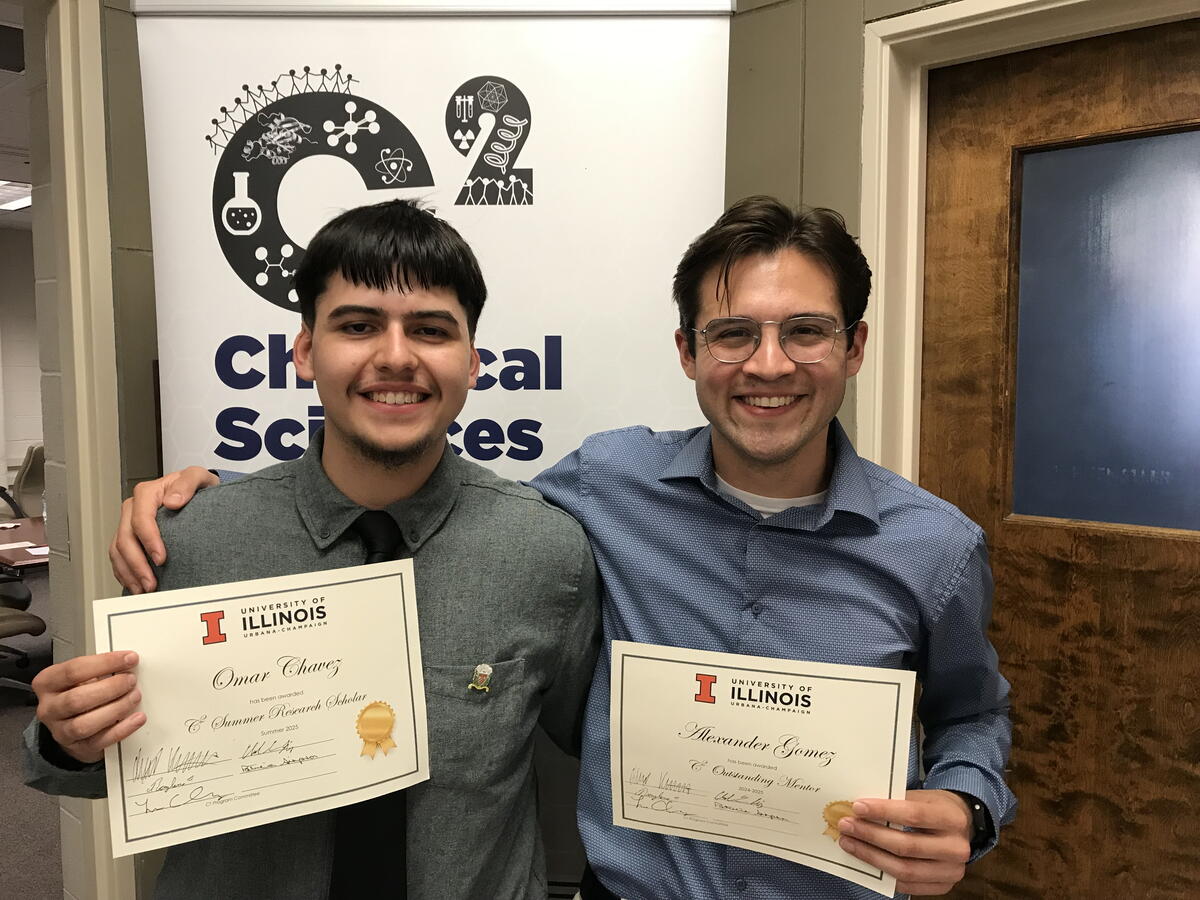 Two students standing side by side in front of a C2 banner holding certificates.
