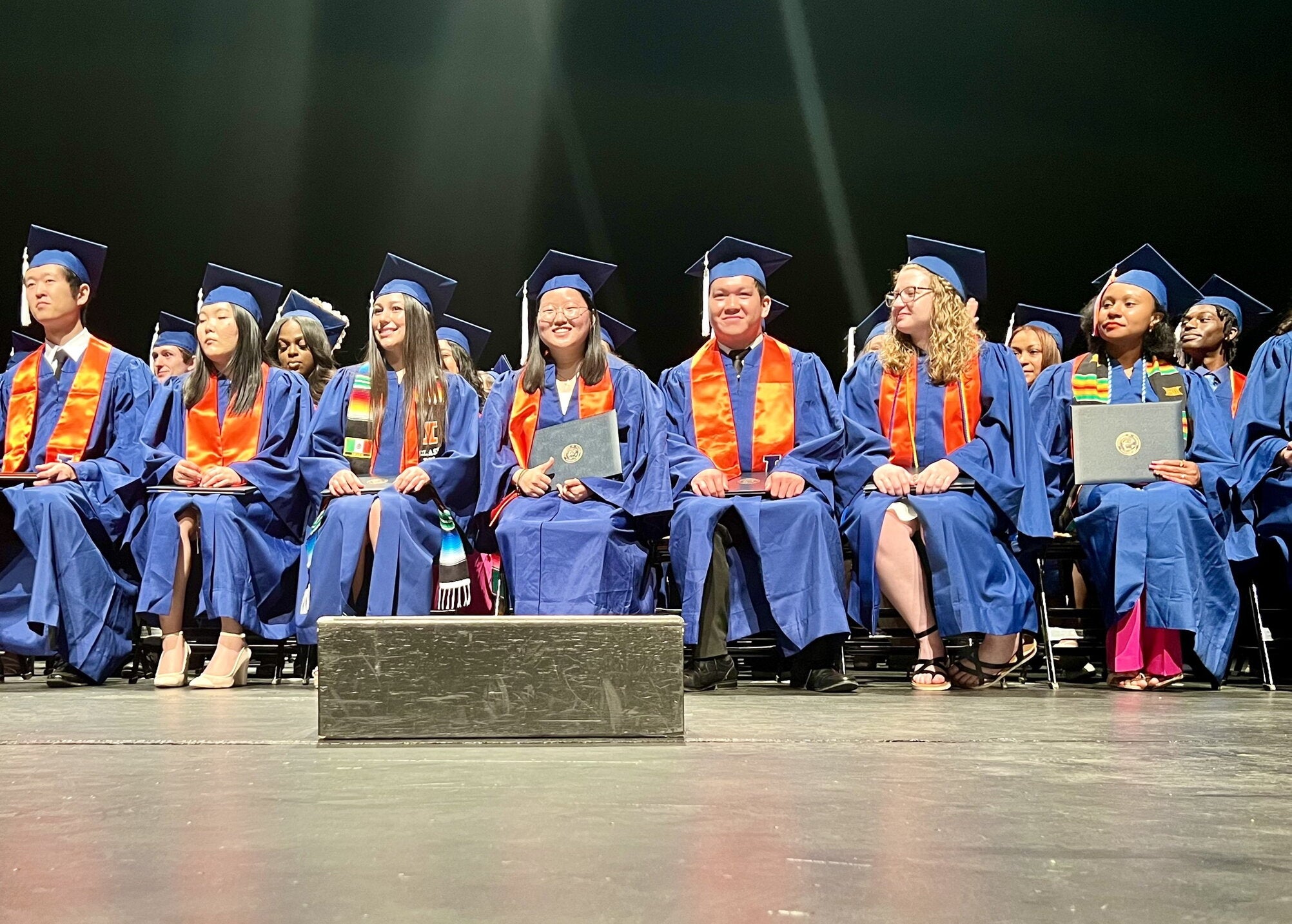 Graduates in regalia sitting in the front row on stage during Convocation.
