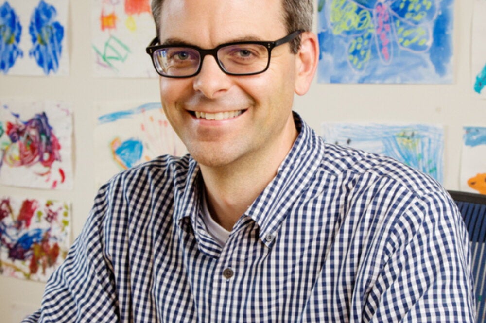 Portrait of Martin Burke seated with a white wall behind him that is full of colorful drawings