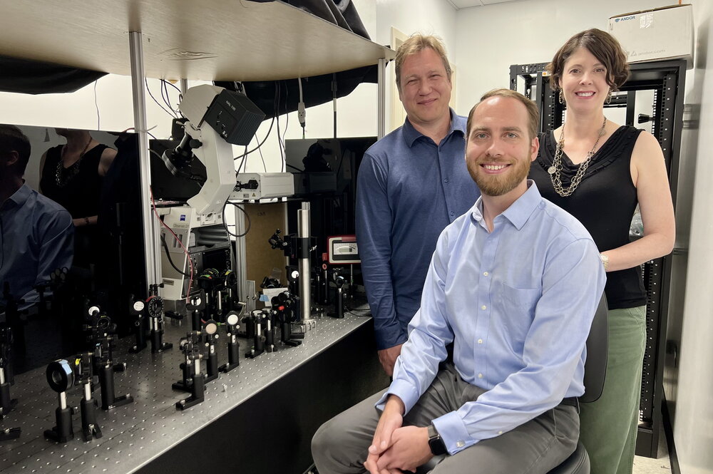 Stephan Link, Stephen Lee, and Christy Landes are pictured in the lab next standing and sitting next to equipment used in their research. 
