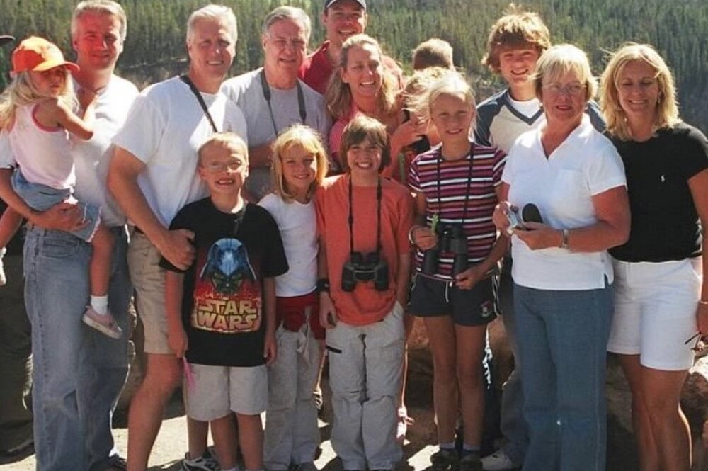 Dr. Milligan and 13 of his family members stand in a group in a location at Yellowstone overlooking a wooded area.