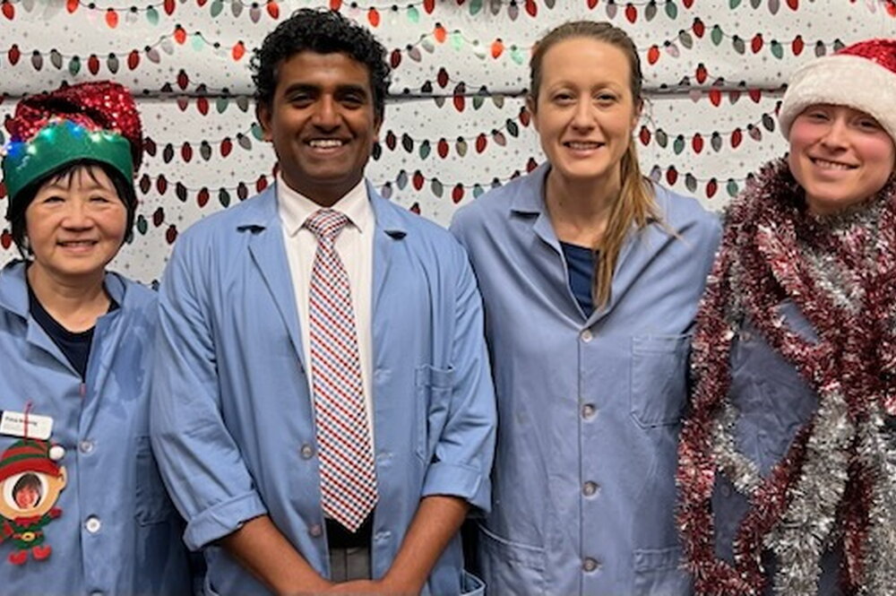 Four people in lab coats and holiday accessories stand side by side