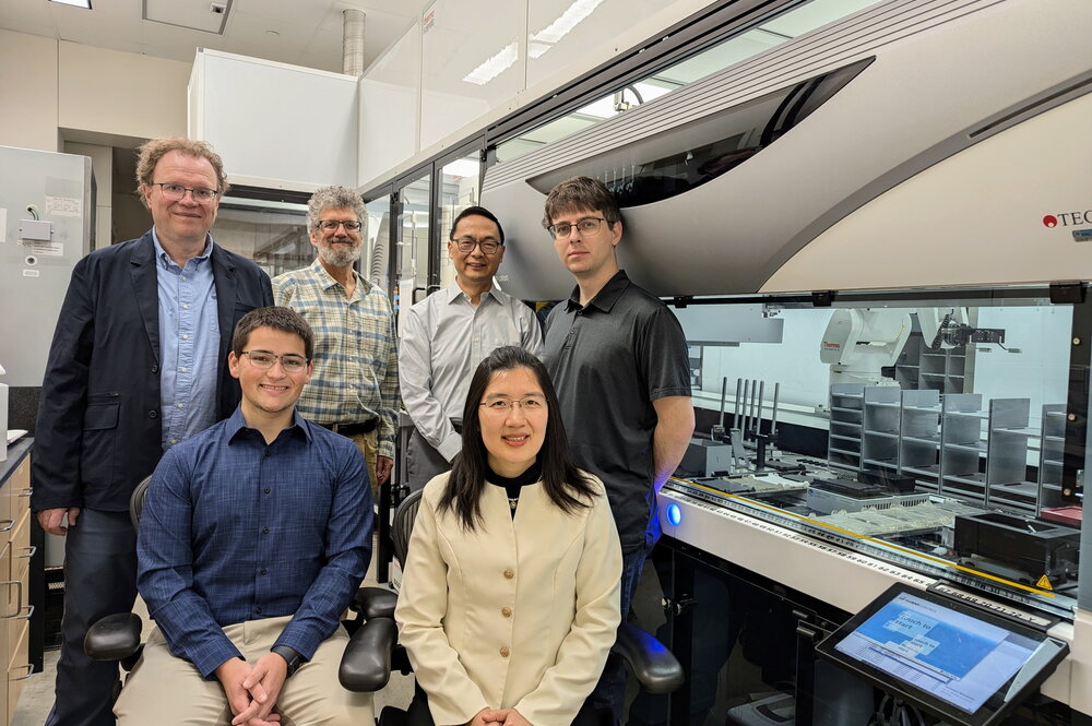 A group of researchers standing/sitting together in a research lab with equipment in the background