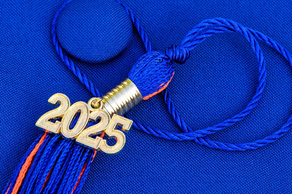 Tassel from a graduation cap laying on top of a blue graduation cap