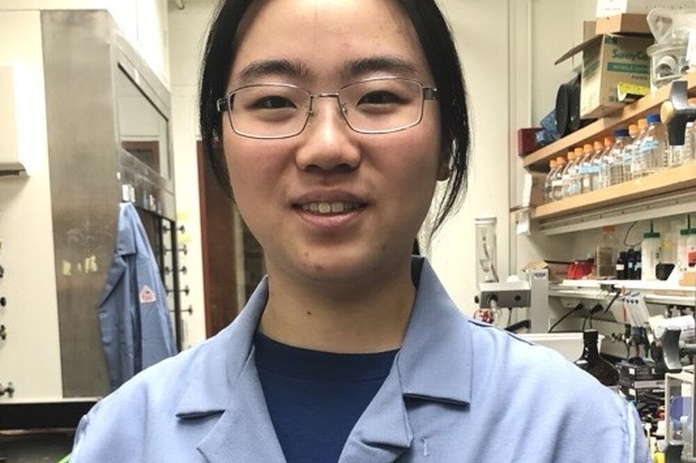 Head shot of Chang Jiang in a blue lab coat in a lab