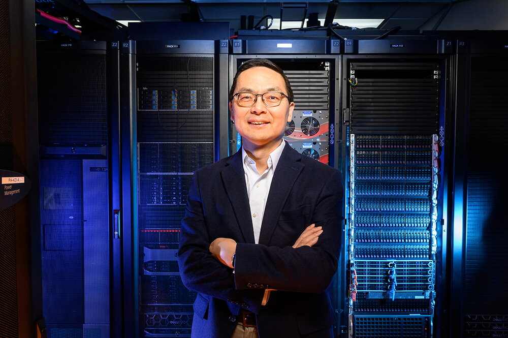 Huimin Zhao standing with arms crossed in front of a large bank of computer data equipment