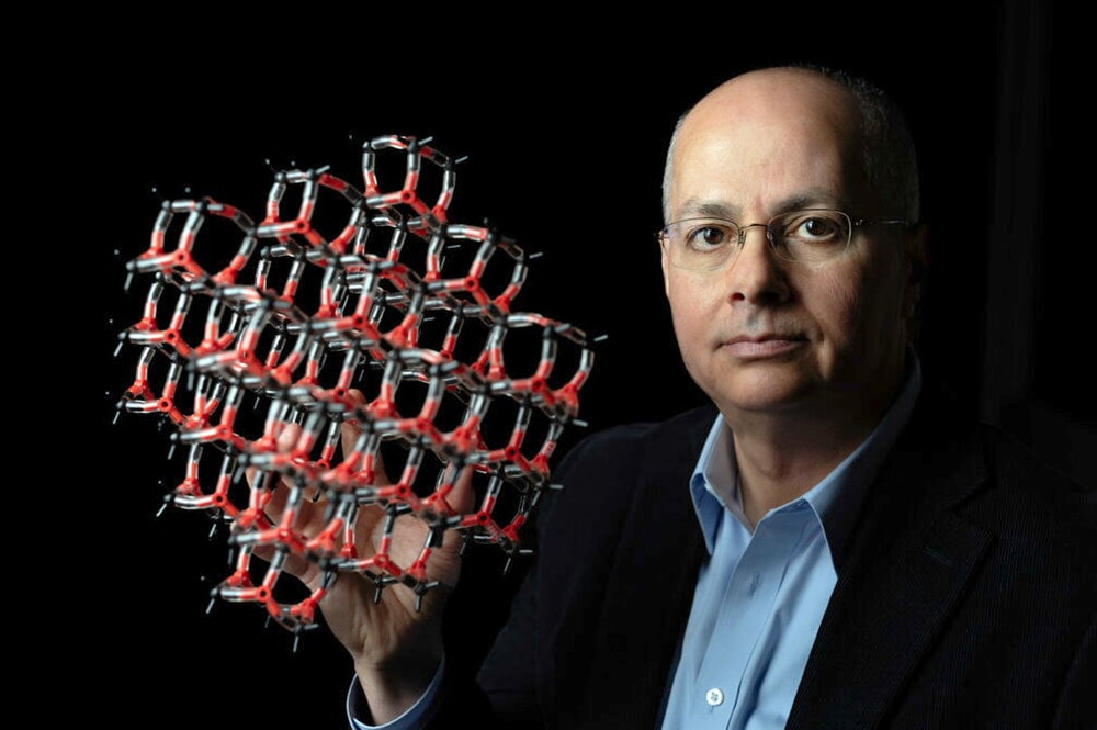 Omar Yaghi holding a molecular structure model on a dark background