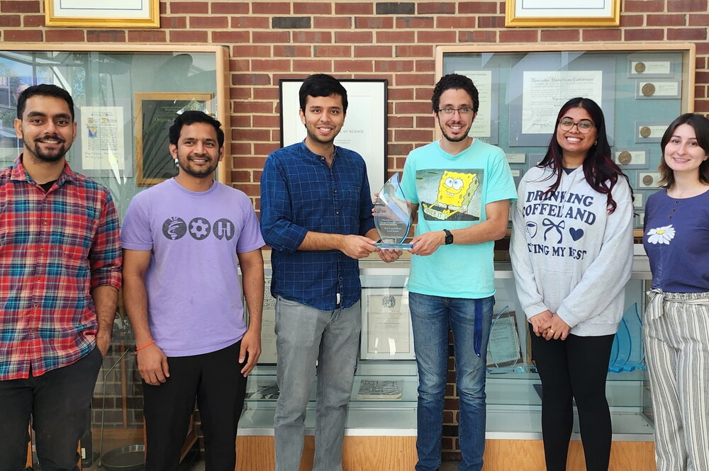 Six people standing side by side with two in middle holding a physical award statue