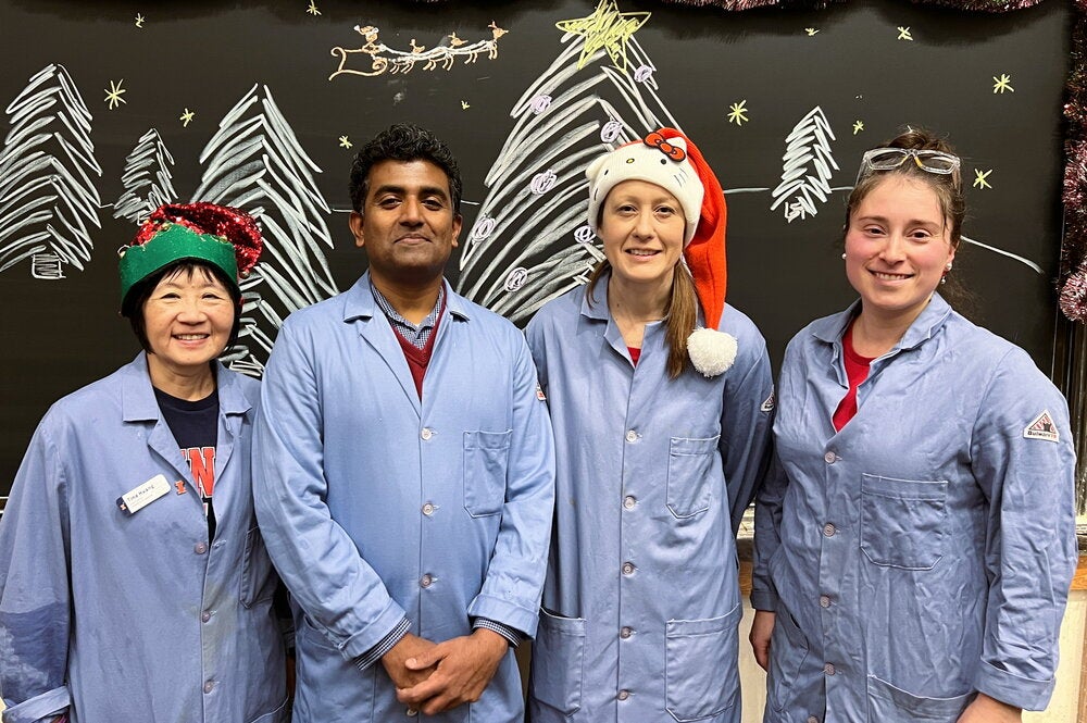 Four people in lab coats standing together in front of a chalk board with christmas trees drawn on the board
