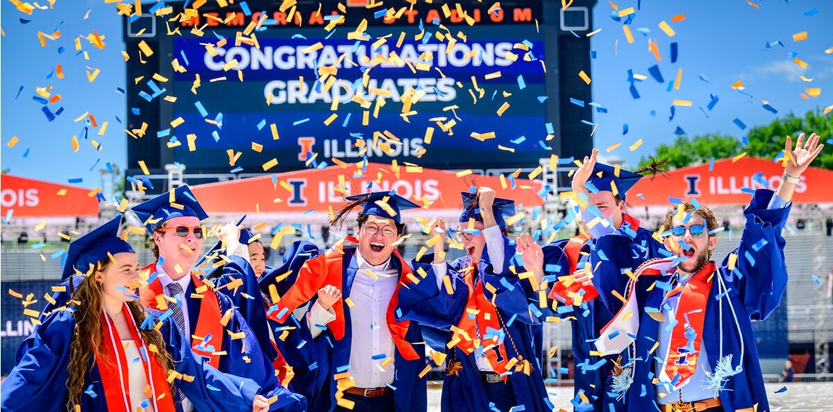 Students in graduation regalia celebrating in the football stadium