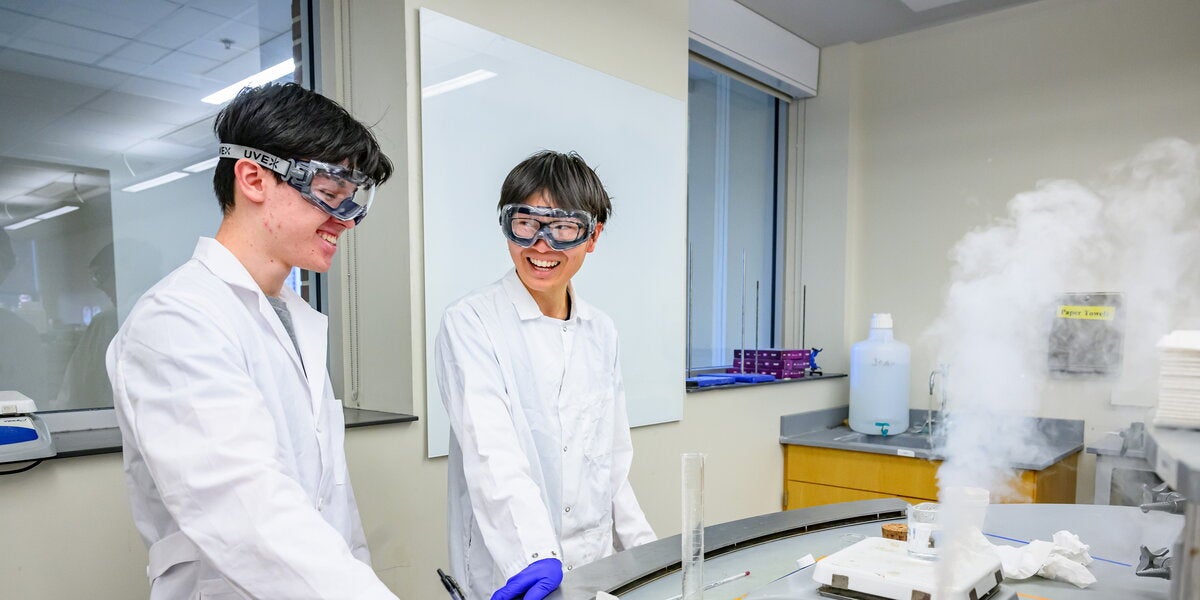 Two students in lab coats and goggles doing a chemistry experiment