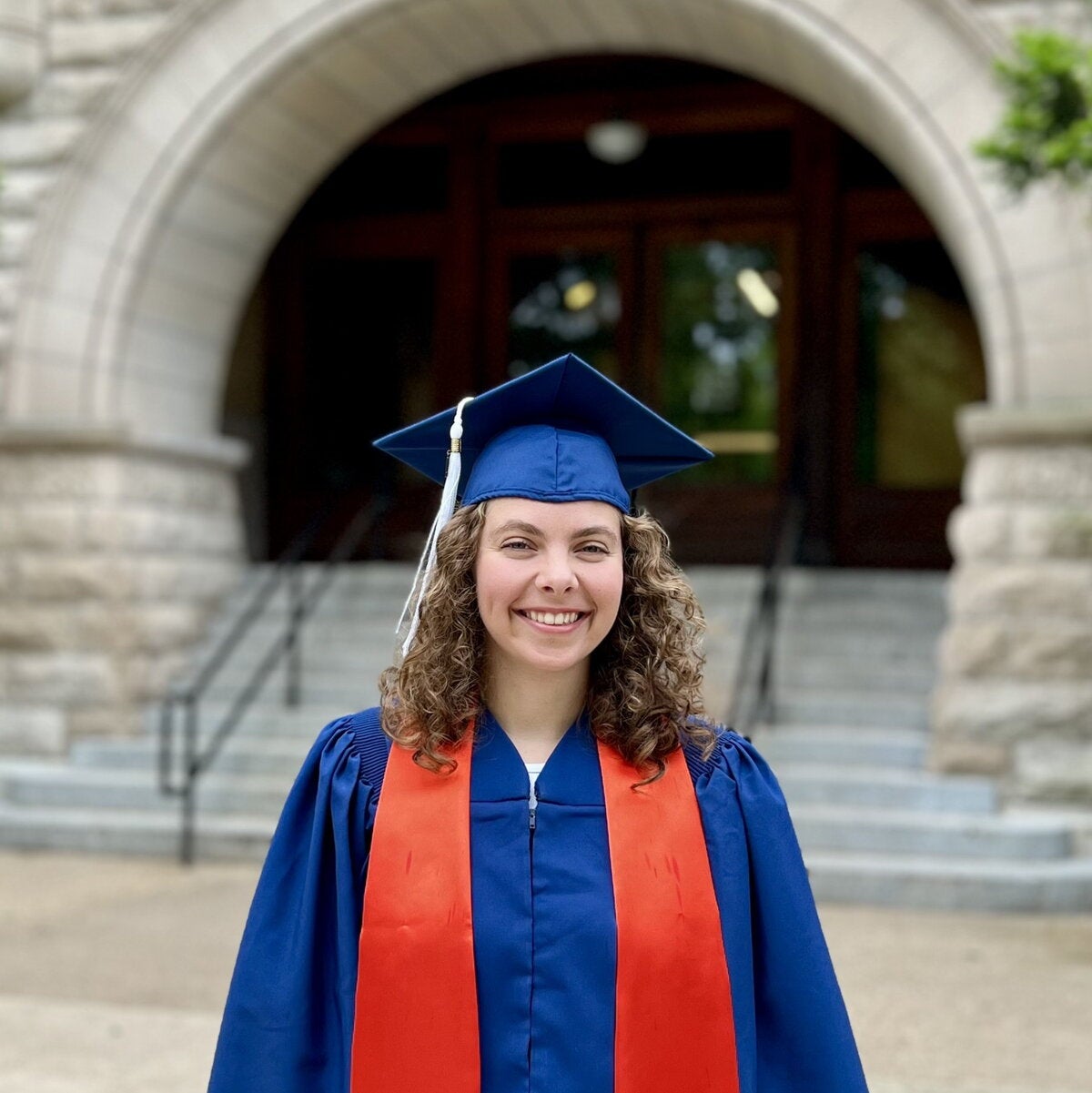 Sofia Sivilotti in a graduation cap and gown standing in front of arched entrance at Noyes Laboratory.  