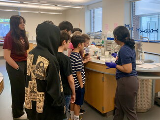 camp leader and kids standing at a chemistry bench in a lab