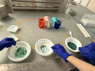 hands touching three paper bowls with colored liquids