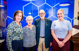Four people standing side by side in front of a bright blue wall. 