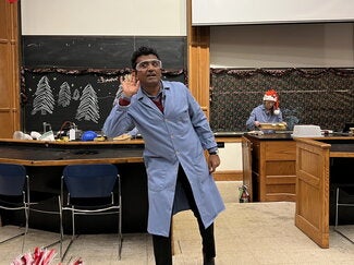 A person in a blue lab coat holding his hear encouraging the audience to speak up so he can hear them