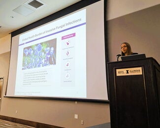 Student at a podium presenting research on a large overhead screen