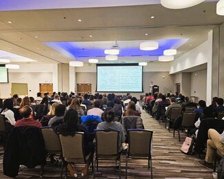 Large conference room filled with people in chairs listening to a presentation