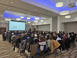 Large conference room filled with people in chairs listening to a presentation