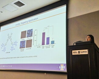 Student at a podium presenting research on a large overhead screen