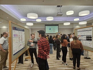 Conference room full of people standing at presentation boards sharing their research