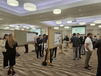 Conference room full of people standing at presentation boards sharing their research