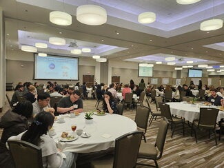 Conference room filled with people sitting at circle tables enjoying lunch