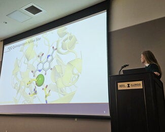 Student at a podium presenting research on a large overhead screen